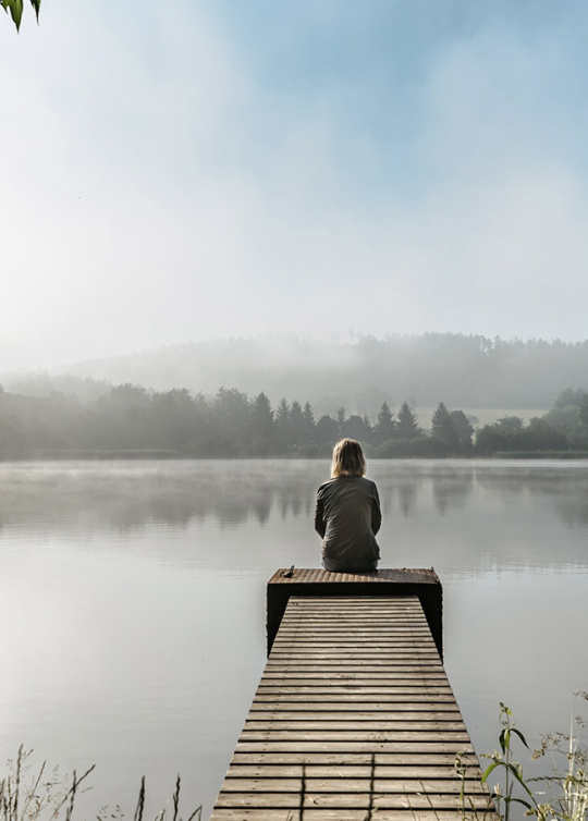 Jeune femme assise au bout qu'un quai en bois regardant un lac