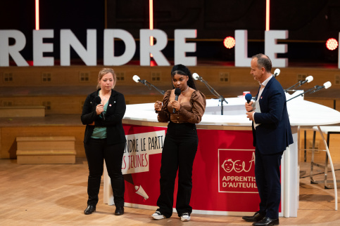 3 personnes sur une scène lors d'un évenement Apprentis d'Auteuil de lancement de son plaidoyer : Prendre le parti des jeunes. 1 jeune fille avec un micro accompagnée d'une éducatrice spécialisée et de Nicolas Truelle, directeur général.