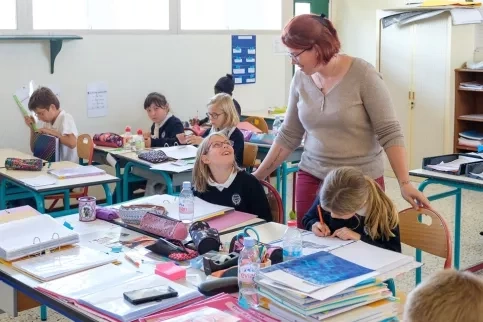 une éducatrice qui fait du suivi scolaire dans une classe de jeunes élèves