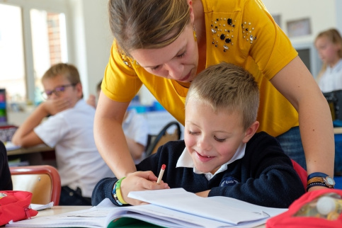 Une professeure des écoles accompagne un jeune élève dans un exercice