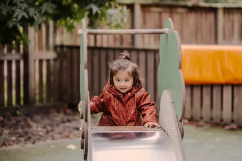 une petite fille joue à l'exterieur dans le jardin sur le toboggan à la crèche