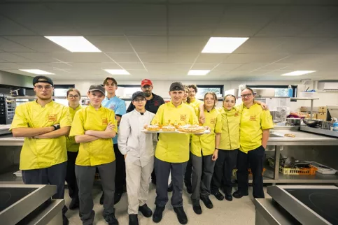 Un groupe d'une dizaine de jeunes en tenue de pâtissiers posent dans leur laboratoire de formation.
