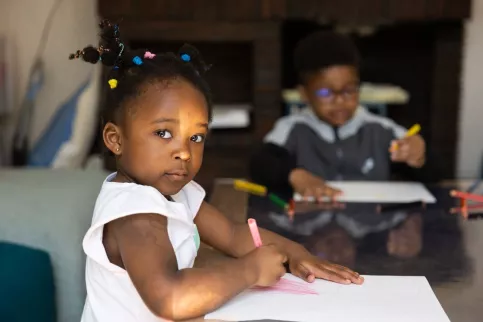 Une petite fille dessine, assise à une table.
