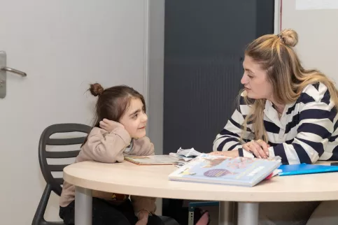 Une petite fille et une adulte sont assises à une table devant des cahiers de devoir