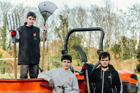 3  jeunes gens en tenue de professionnels des travaux paysagers devant un camion