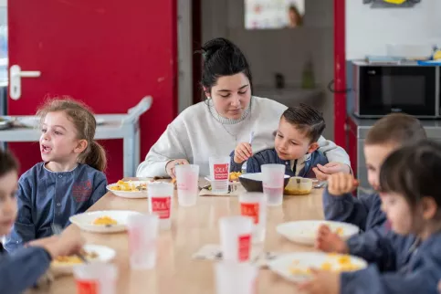 Des enfants et une jeune femme assis à une table de déjeuner