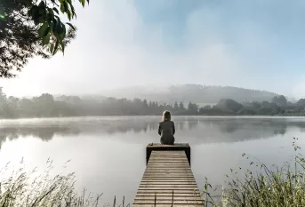 Jeune femme assise au bout qu'un quai en bois regardant un lac