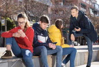 Adolescents assis sur un muret, deux d'entre eux discutent et deux autres sont sur leur téléphone portable