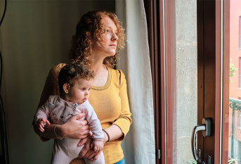 Une maman portant son bébé dans ses bras et regardant par la fenêtre de son appartement