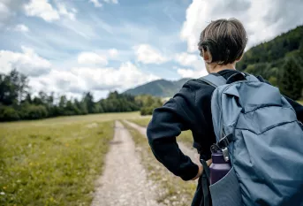 Jeune, de dos, avec un sac à dos face à une route de campagne