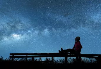 Jeune femme assise sur un banc regardant un ciel étoilé