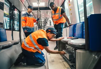 Ayoub est accompagné par la Fondation Apprentis d'Auteuil dans le cadre d'un programme d'apprentissage SKOLA "Technicien de maintenance industrielle ferroviaire". Il est avec son tuteur d'apprentissage, Cédric Ntietie, chef de dépôt du site RATP MP14 et Eric, un étudiant en apprentissage; ils vérifient le fonctionnement du système de vidéo surveillance dans une rame MP14