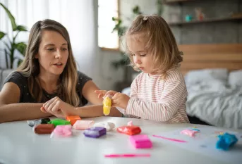 Une petite fille fait de la pâte à modeler sous l'oeil de sa maman