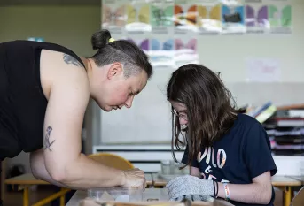 Graines d'artistes-Petits compagnons - Séance de pratique artistique au collège Sainte-Claire dans le cadre du projet artistique en lien avec la Fondation Foujita. La séance est encadrée par Annabelle Bichard, intervenante. Annabelle donne des conseils à Charlotte qui taille une pierre en forme de coeur pour sa maman.
