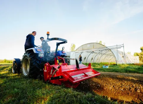 Un apprenti et un enseignant sur un tracteur devant une serre