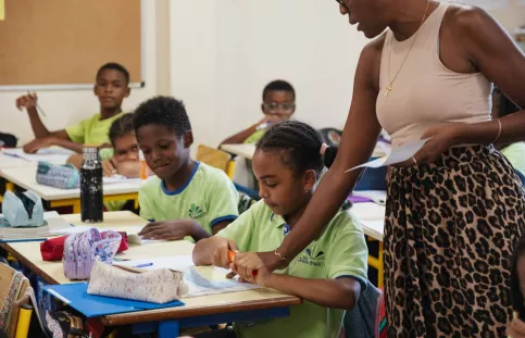 Dans une salle de classe, une professeure des écoles debout près d'élèves assis