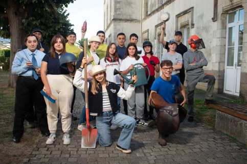 Un groupe de jeunes pose, certains tenant un objet symbolisant sa formation : pelle, casque de soudeur, casserole, légume...
