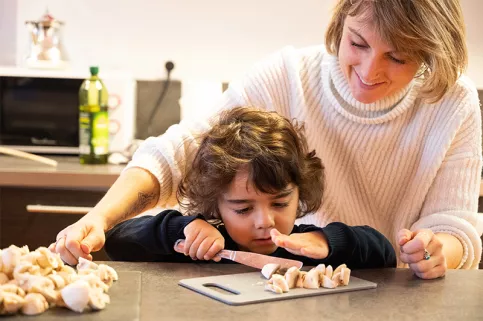 Thays, 4 ans, à l'accueil éducatif de jour Louis et Zélie Martin de Colmar coupe des champignons sous le regard de Laëtitia Simonutti, maîtresse de maison 