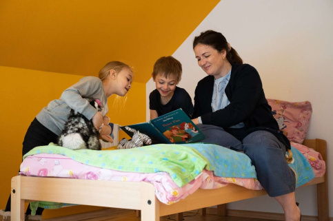 Dans une chambre d'enfants, 2 enfants avec une éducatrice font la lecture.
