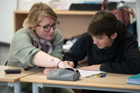 Une jeune femme travaille avec un jeune collégien côte à côte.
