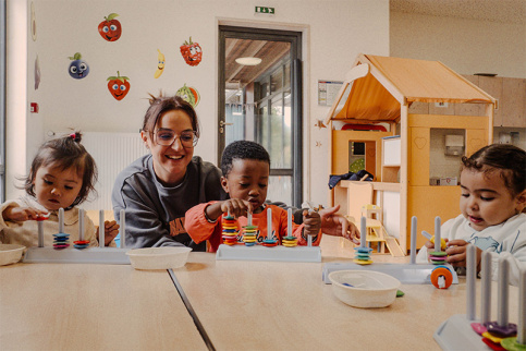 Crèche Les petites pousses du lac - Atelier motricité fine pour les moyens grâce un jeu de précision. Emeline Lima accompagne Ava et Bilal dans l'activité