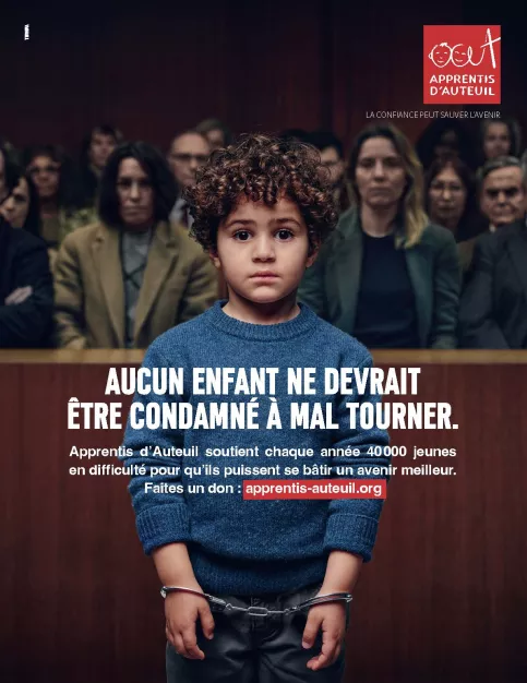 Un petit garçon d'environ 4 ans est menotté dans un tribunal. On voit derrière lui le public un peu flouté. Texte : Aucun enfant ne devrait être condamné à mal tourner. Apprentis d'Auteuil soutient chaque année 40 000 jeunes en difficulté pour qu'ils puissent se bâtir un avenir meilleur. Faites un don sur www.apprentis-auteuil.org