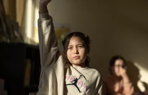Une petite fille assise en classe lève le doigt