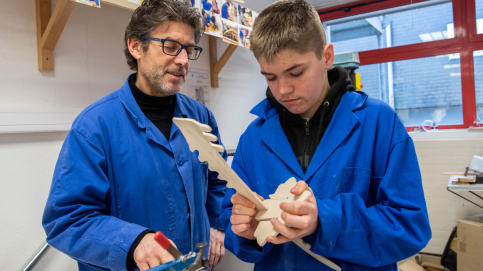 Kylian termine son oeuvre sous l'oeil attentif de Julio Correia, éducateur technique à l'atelier bois