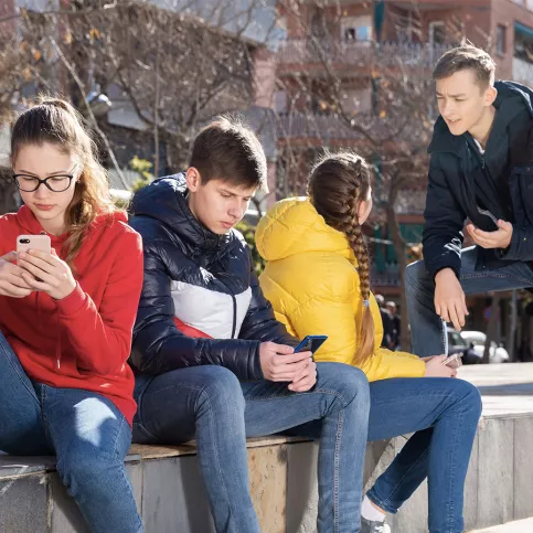 Adolescents assis sur un muret, deux d'entre eux discutent et deux autres sont sur leur téléphone portable