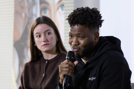 Un jeune homme parle au micro. A sa droite, une jeune fille le regarde. 