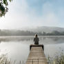 Jeune femme assise au bout qu'un quai en bois regardant un lac